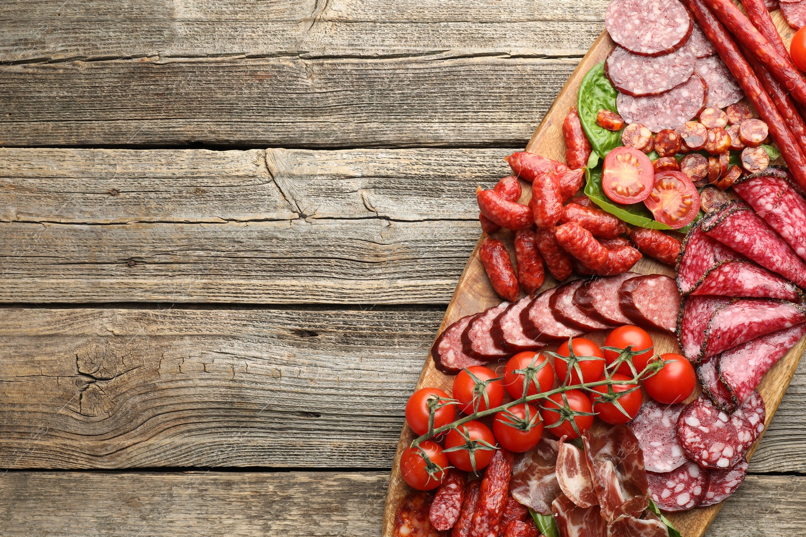 Photo of Different smoked sausages, ham and tomatoes on wooden table, top view. Space for text