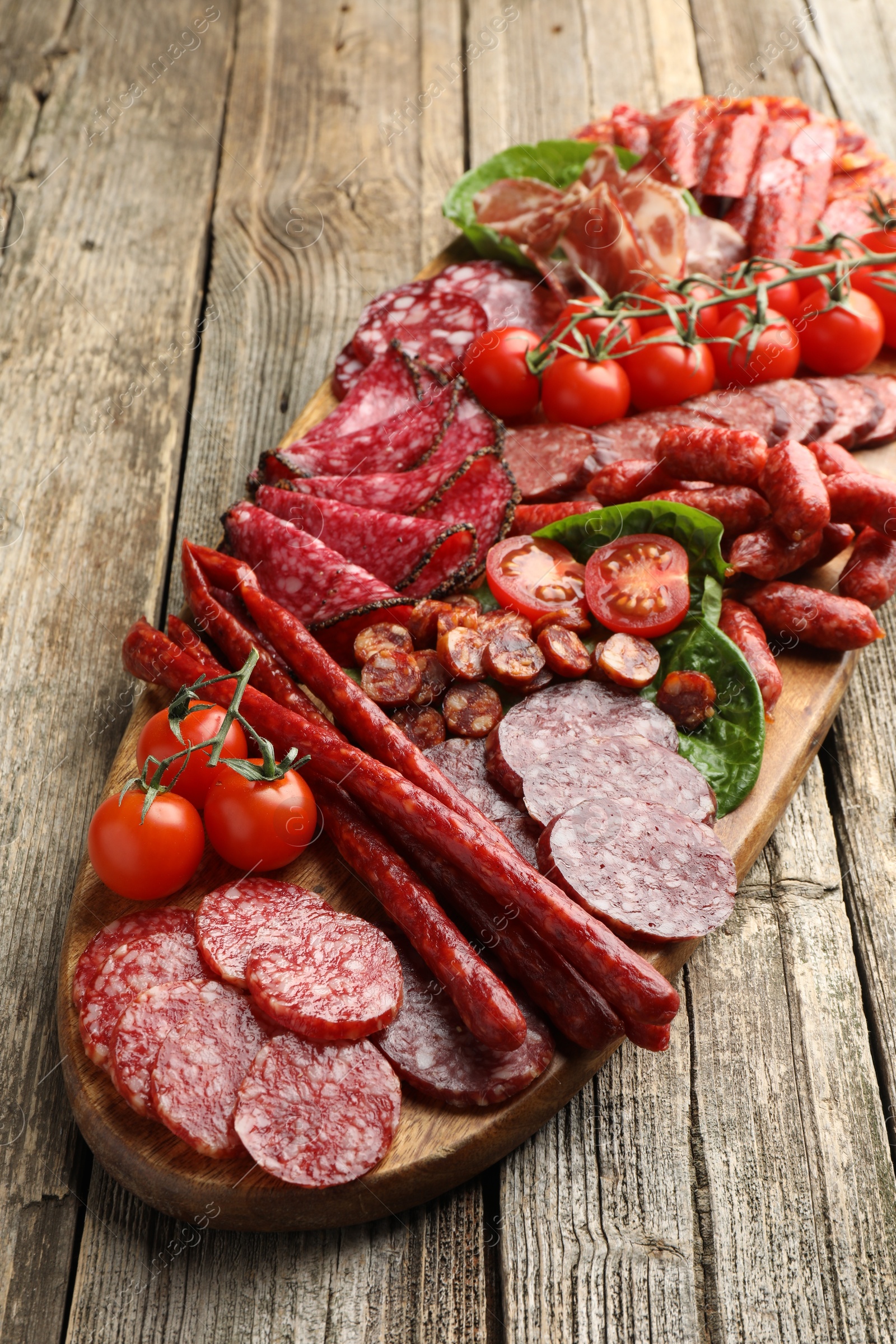 Photo of Different smoked sausages, ham and tomatoes on wooden table, closeup