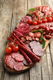 Photo of Different smoked sausages, ham and tomatoes on wooden table, closeup