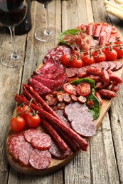 Photo of Different smoked sausages, tomatoes, ham and wine on wooden table, closeup