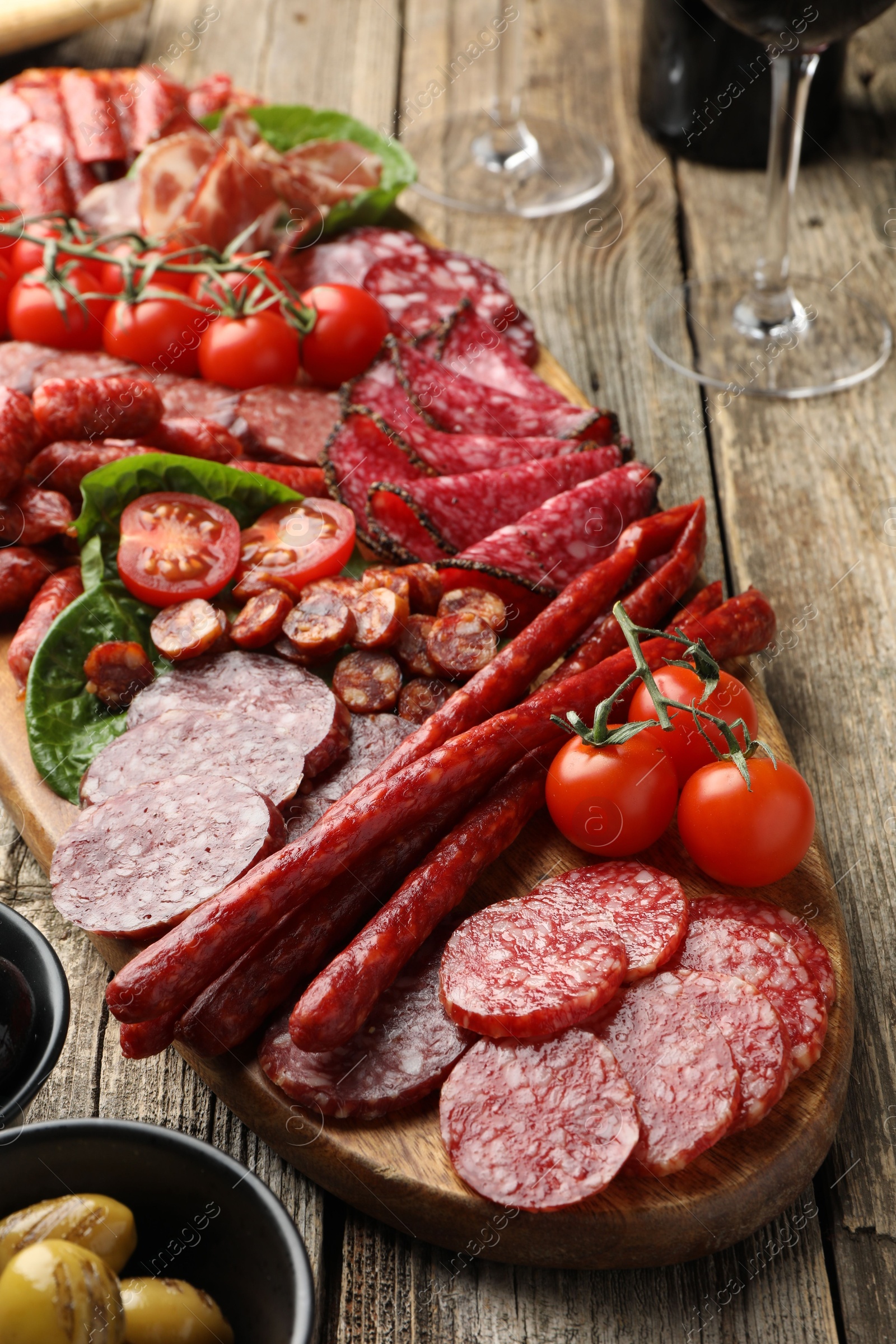 Photo of Different smoked sausages and other snacks served on wooden table, closeup