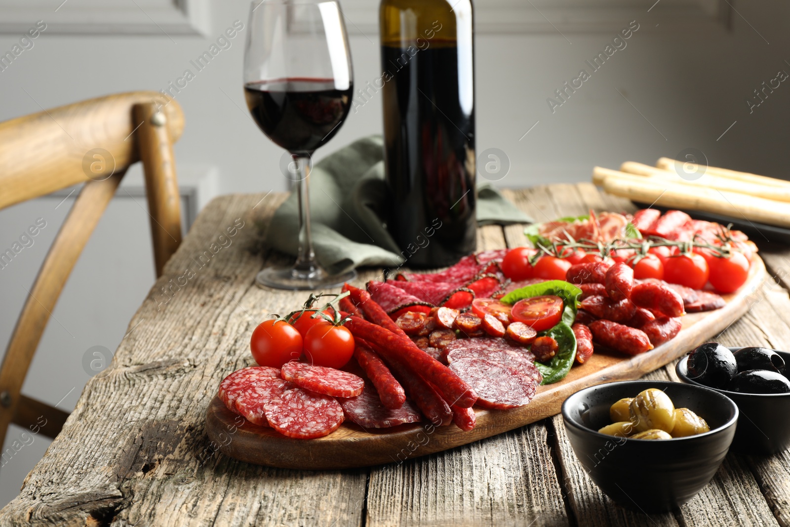 Photo of Different smoked sausages and other snacks served with wine on wooden table, closeup