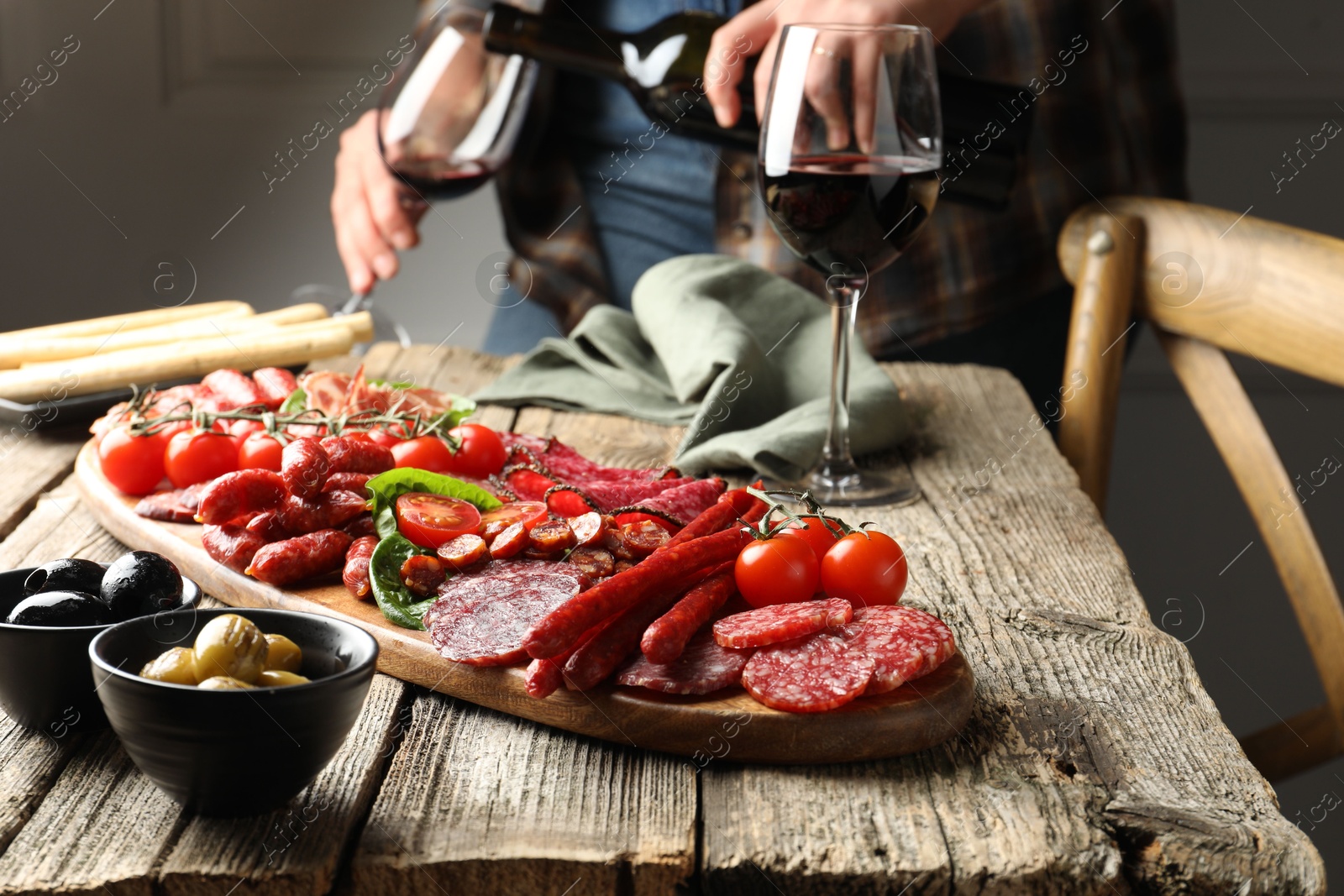 Photo of Woman pouring wine into glass at wooden table with different smoked sausages, selective focus