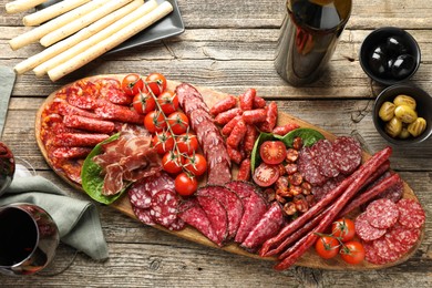 Photo of Different smoked sausages and other snacks served with wine on wooden table, flat lay