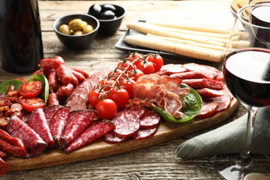 Photo of Different smoked sausages and other snacks served with wine on wooden table, closeup