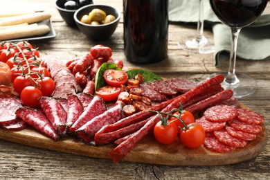 Photo of Different smoked sausages and other snacks served with wine on wooden table, closeup