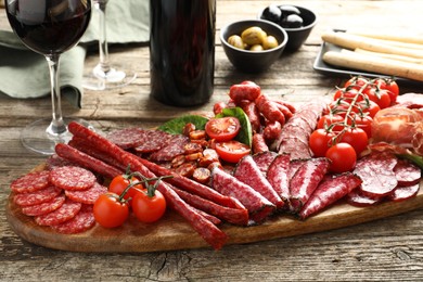 Photo of Different smoked sausages and other snacks served with wine on wooden table, closeup