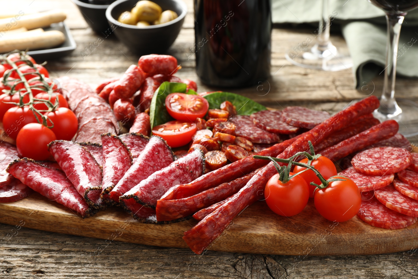 Photo of Different smoked sausages and other snacks served on wooden table, closeup