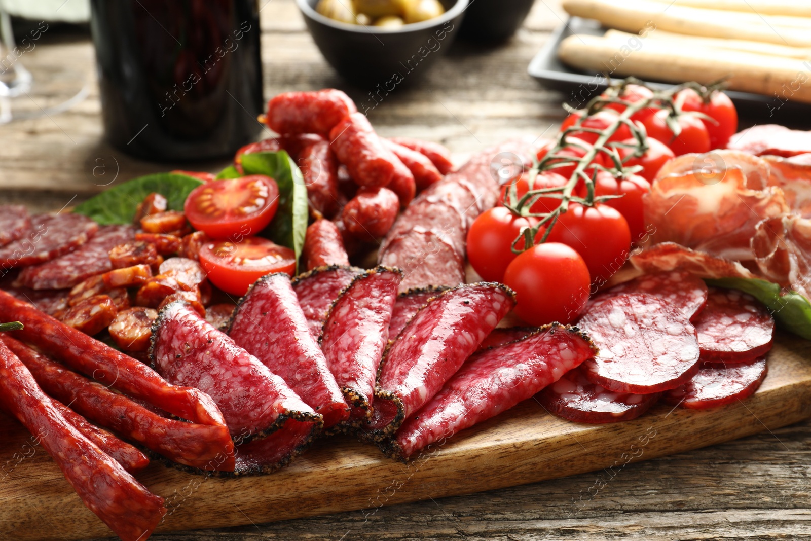 Photo of Different smoked sausages and other snacks served on wooden table, closeup