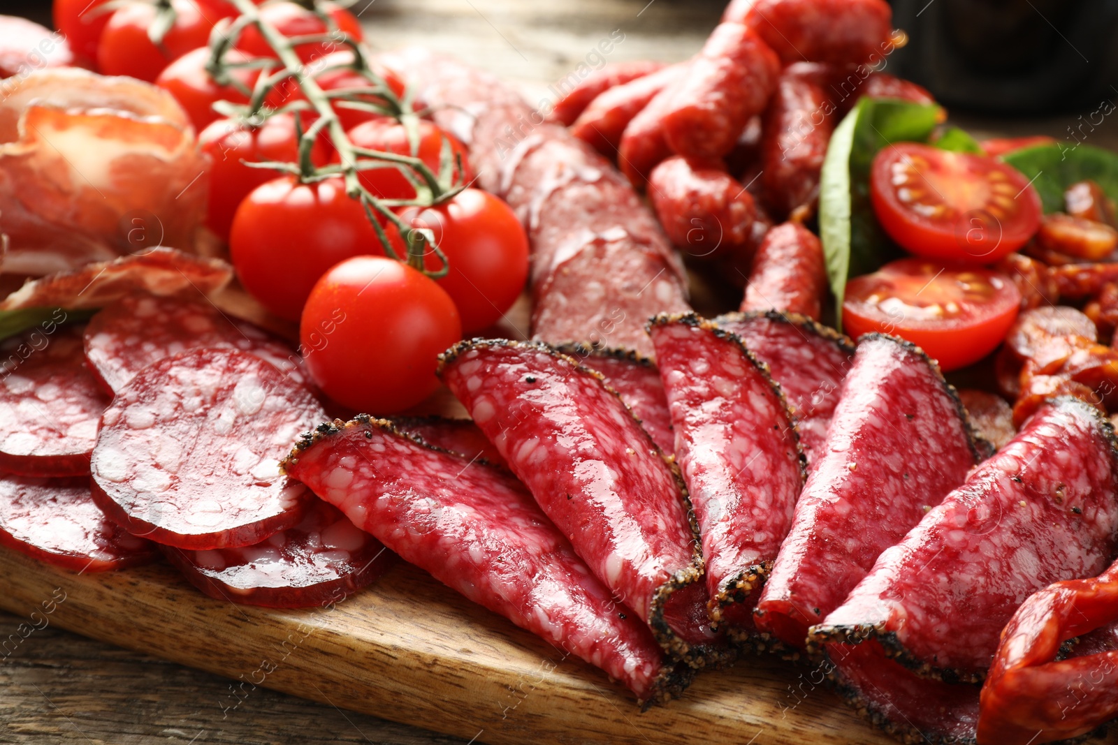 Photo of Different smoked sausages, ham and tomatoes on table, closeup