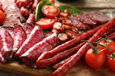 Photo of Different smoked sausages and tomatoes on table, closeup