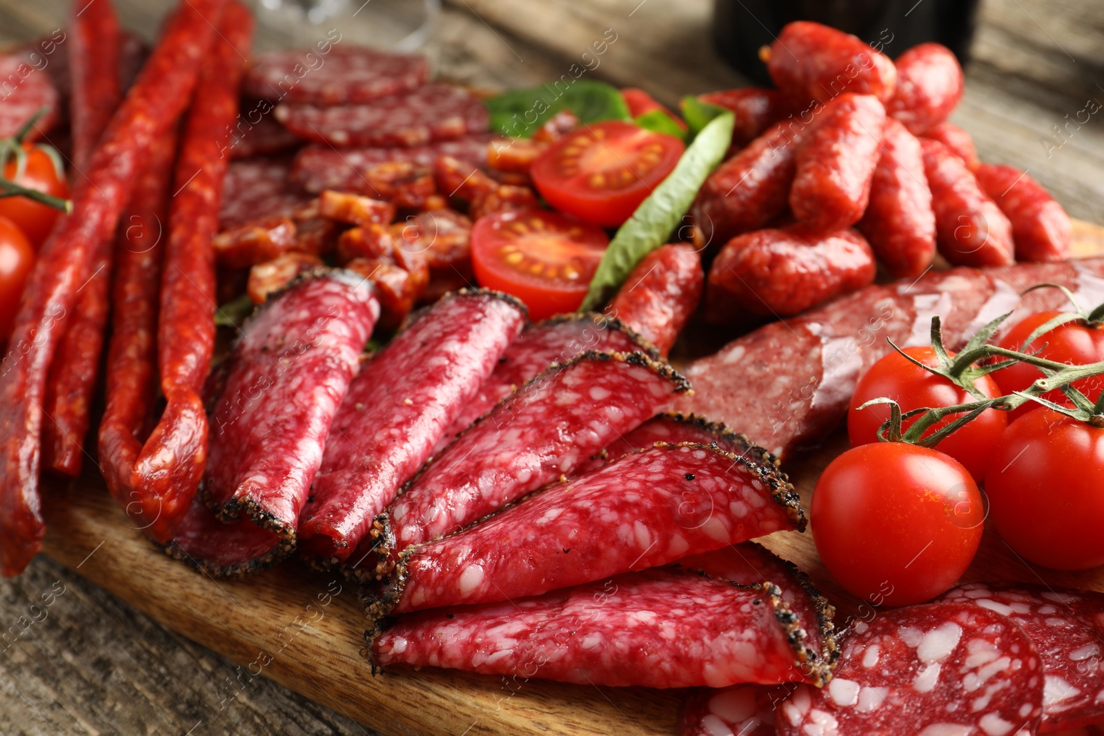 Photo of Different smoked sausages and tomatoes on table, closeup