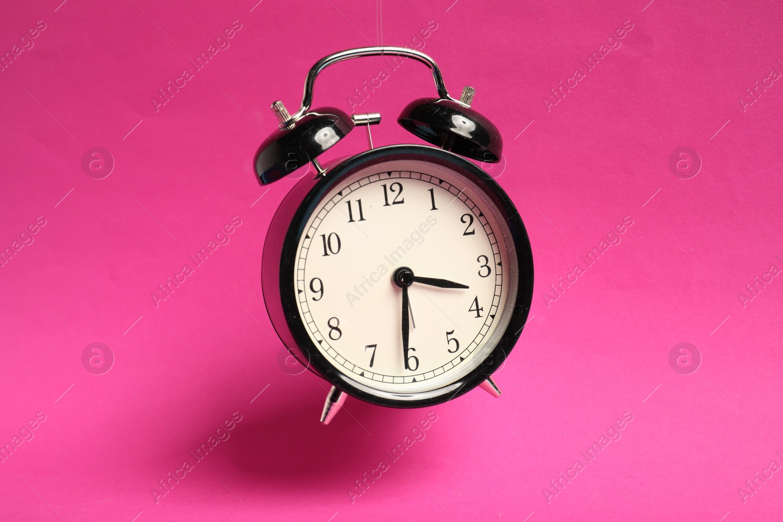 Photo of Black alarm clock in air on bright pink background