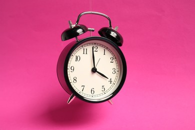 Photo of Black alarm clock in air on bright pink background