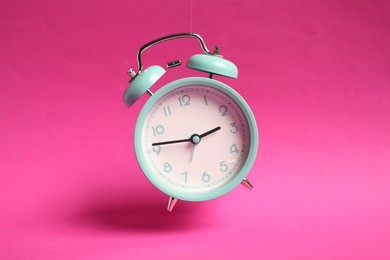 Photo of Turquoise alarm clock in air on bright pink background