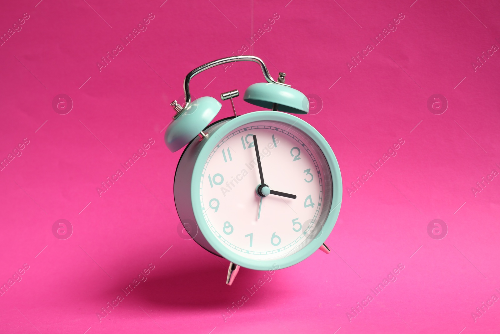 Photo of Turquoise alarm clock in air on bright pink background