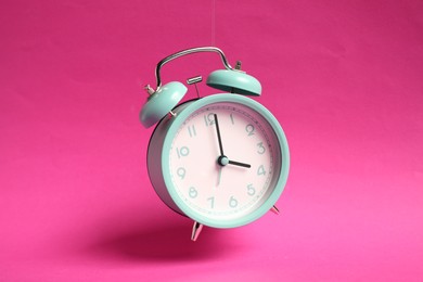 Photo of Turquoise alarm clock in air on bright pink background