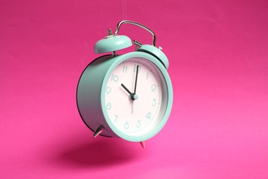 Photo of Turquoise alarm clock in air on bright pink background