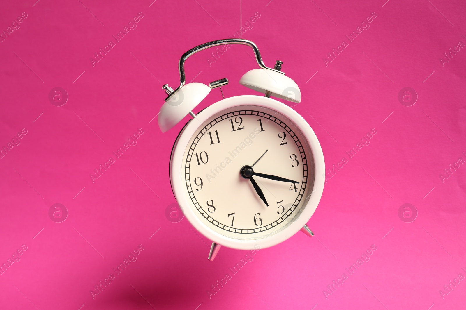 Photo of White alarm clock in air on bright pink background