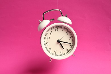 Photo of White alarm clock in air on bright pink background