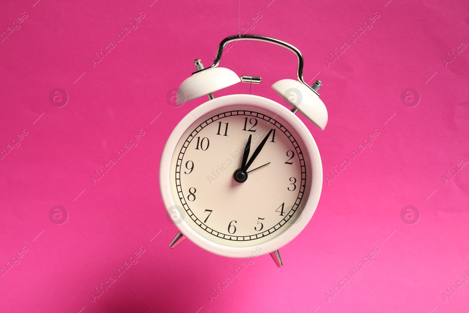 Photo of White alarm clock in air on bright pink background