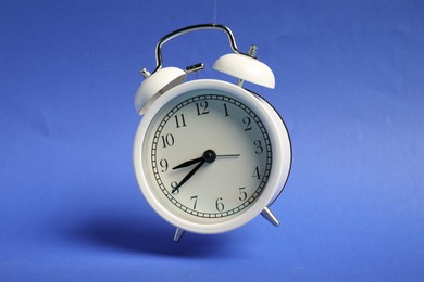 Photo of White alarm clock in air on blue background