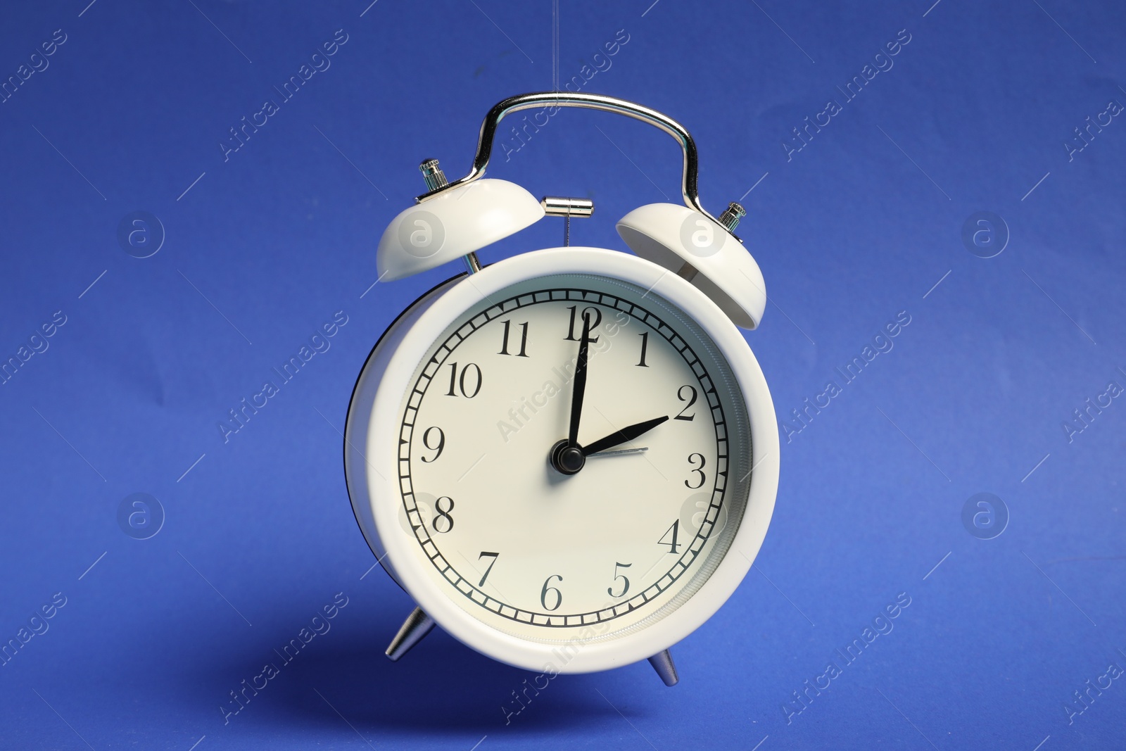 Photo of White alarm clock in air on blue background