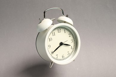 Photo of White alarm clock in air on light grey background