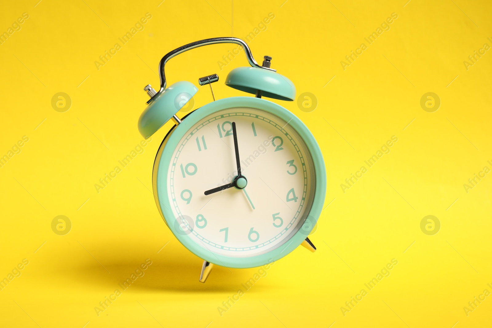 Turquoise alarm clock in air on yellow background Photo of Turquoise alarm clock in air on yellow background