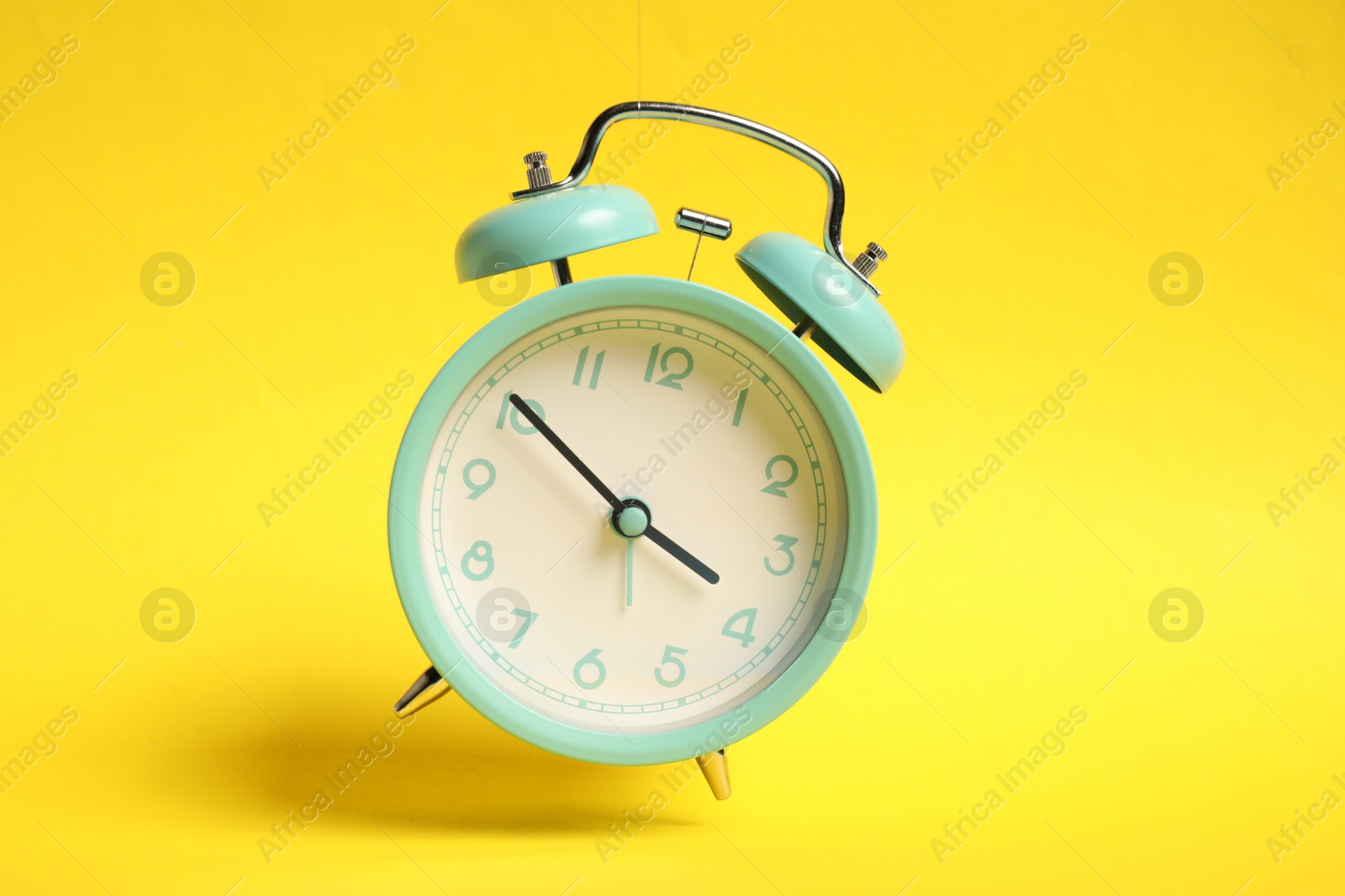 Photo of Turquoise alarm clock in air on yellow background