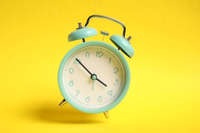 Photo of Turquoise alarm clock in air on yellow background