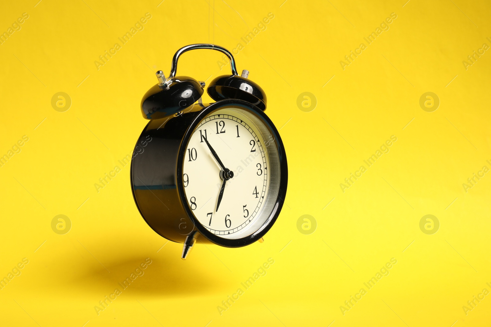 Photo of Black alarm clock in air on yellow background, space for text