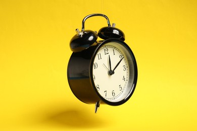 Photo of Black alarm clock in air on yellow background