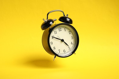 Photo of Black alarm clock in air on yellow background