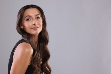 Photo of Hair styling. Portrait of beautiful woman with wavy long hair on grey background, space for text