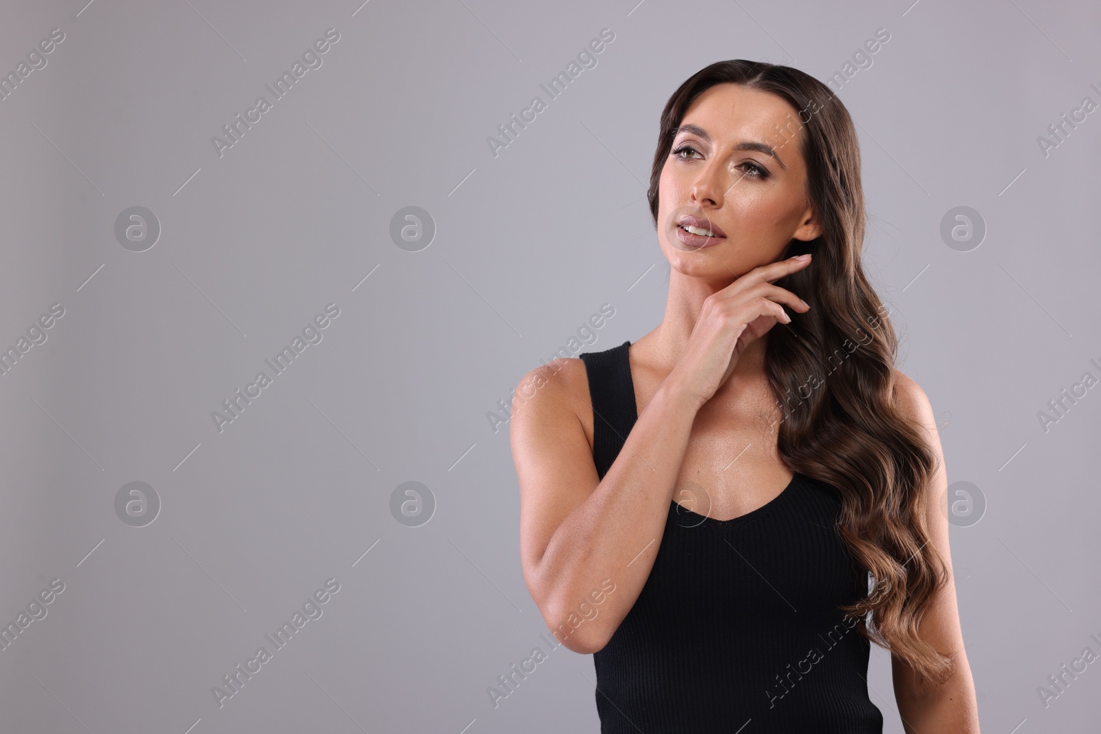 Photo of Hair styling. Beautiful woman with wavy long hair on grey background, space for text