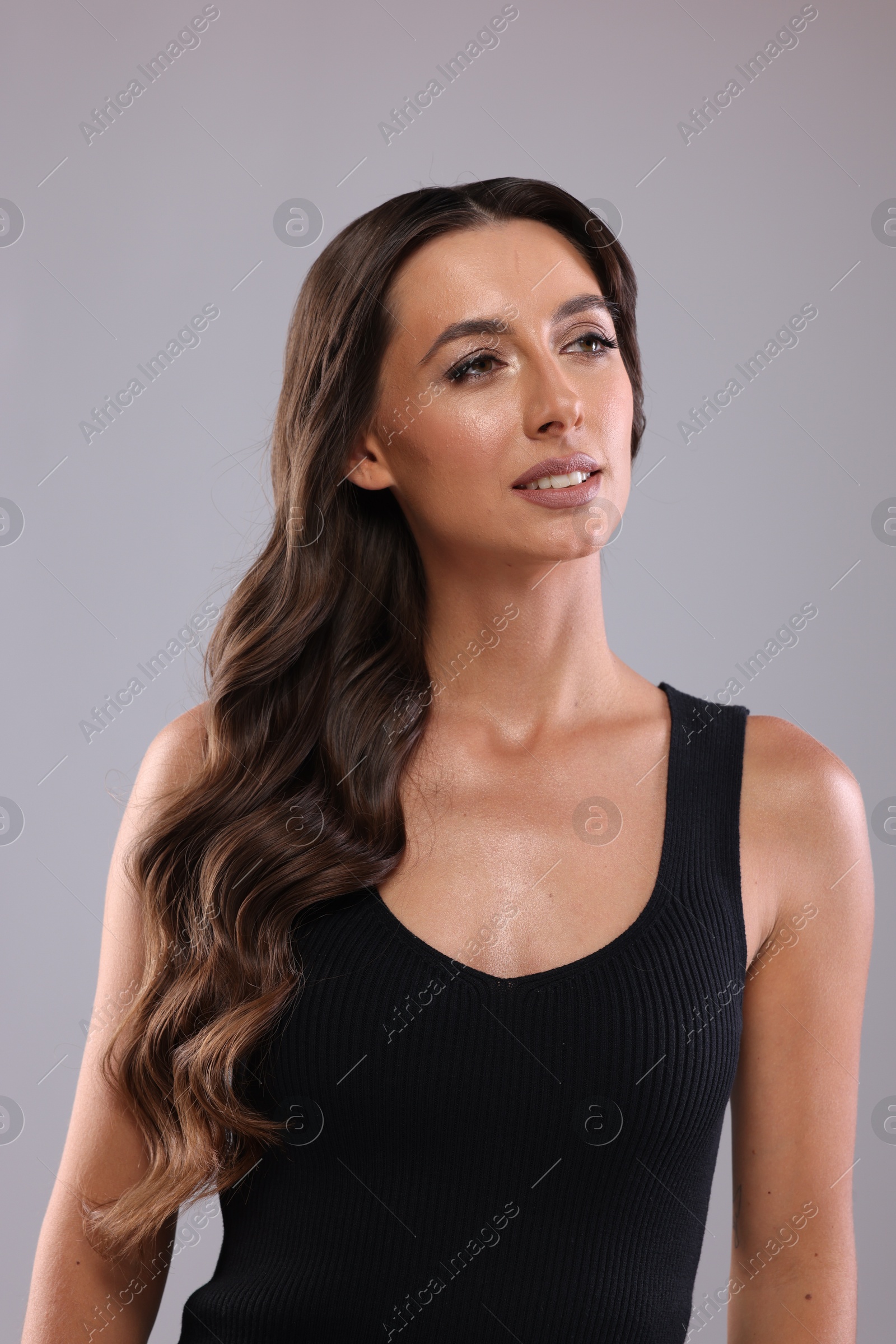 Photo of Hair styling. Beautiful woman with wavy long hair on grey background