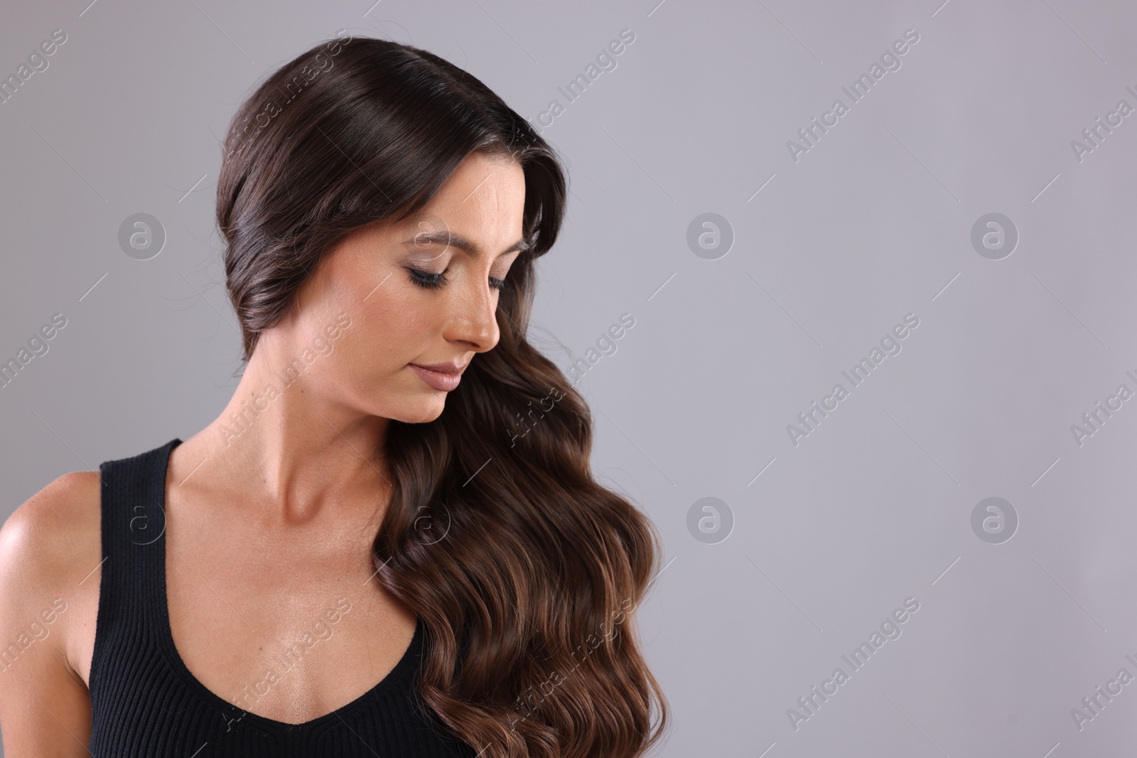 Photo of Hair styling. Beautiful woman with wavy long hair on grey background, space for text