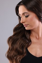 Photo of Hair styling. Beautiful woman with wavy long hair on grey background