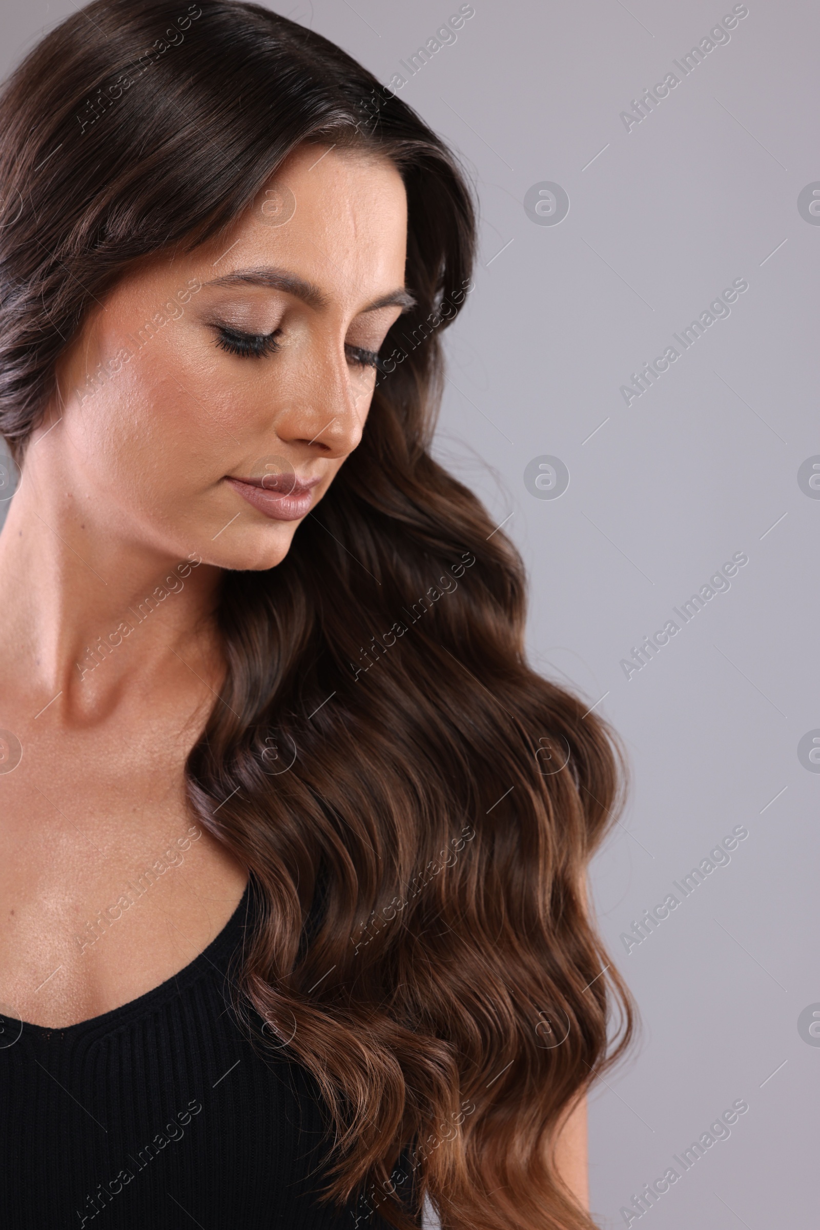 Photo of Hair styling. Beautiful woman with wavy long hair on grey background