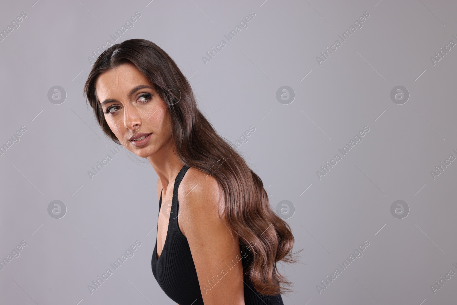 Photo of Hair styling. Beautiful woman with wavy long hair on grey background, space for text