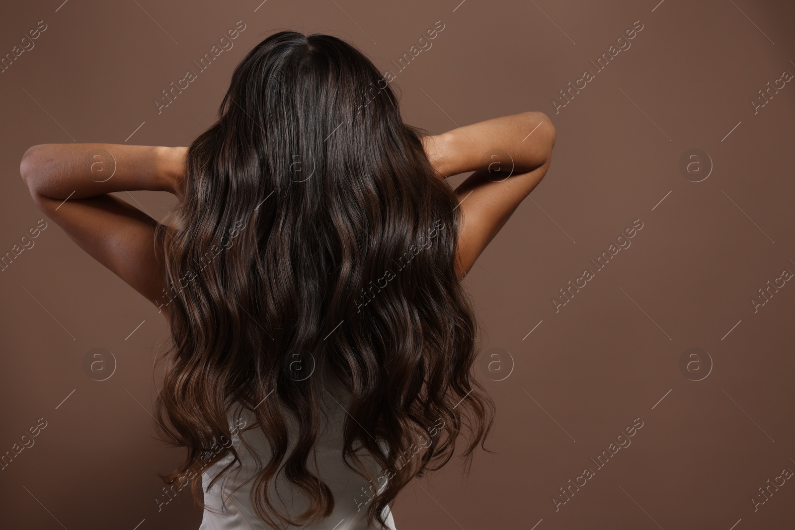 Photo of Hair styling. Woman with wavy long hair on brown background, back view