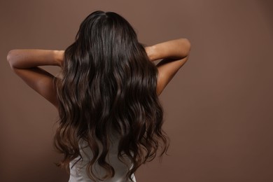 Photo of Hair styling. Woman with wavy long hair on brown background, back view