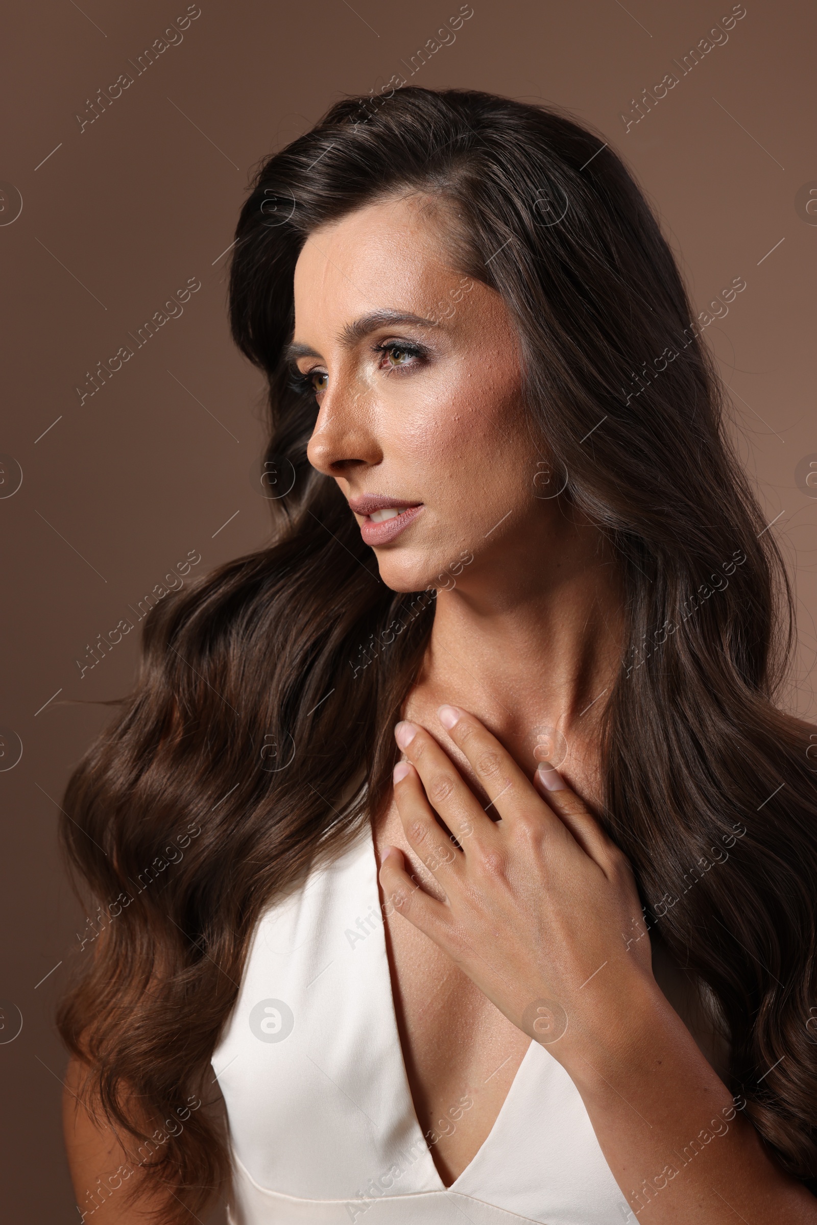 Photo of Hair styling. Beautiful woman with wavy long hair on brown background