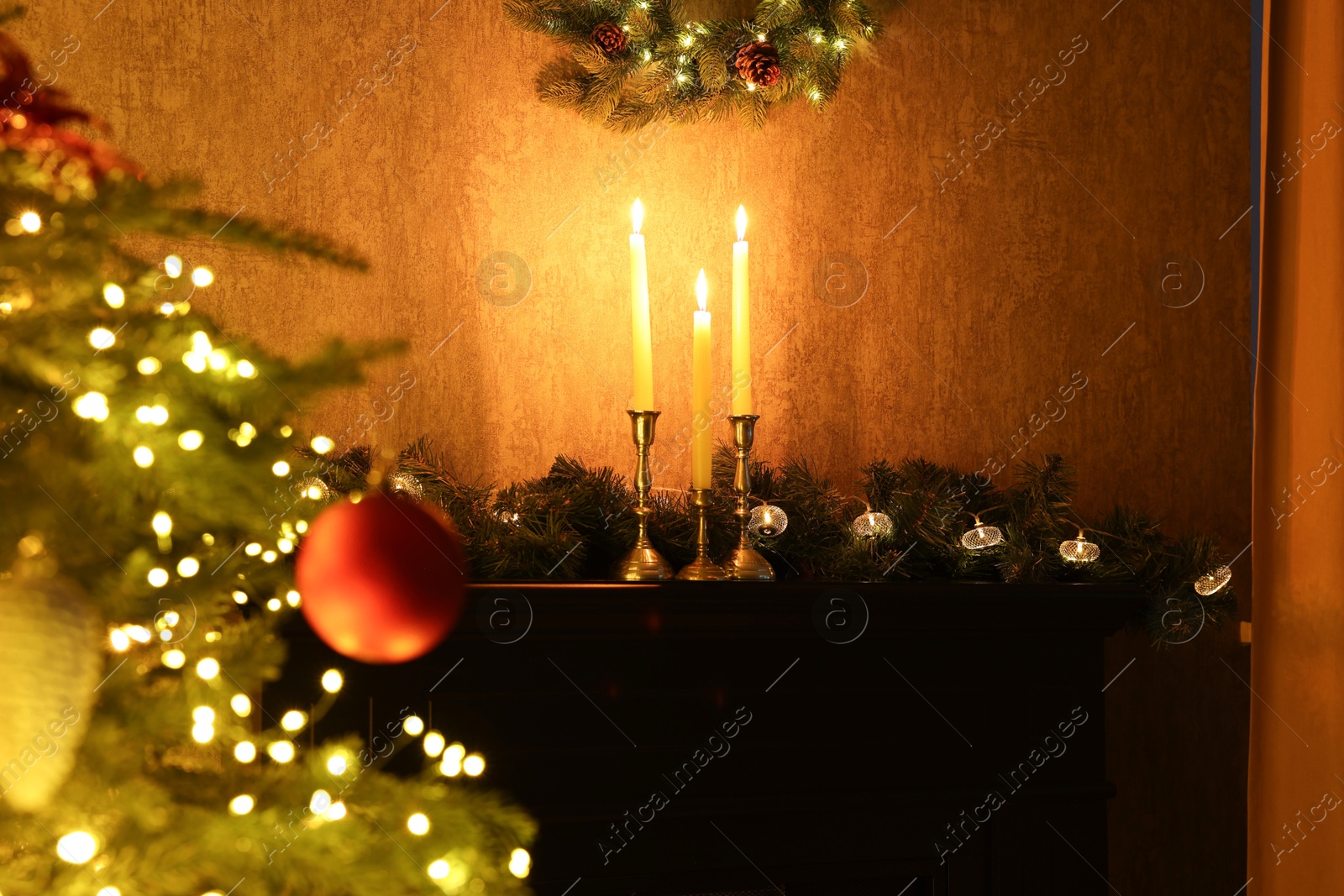 Photo of Beautifully decorated Christmas tree, burning candles and garland indoors, selective focus