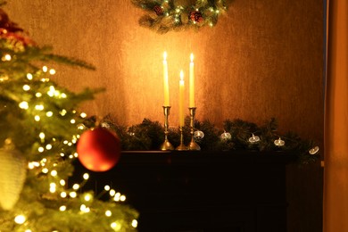 Photo of Beautifully decorated Christmas tree, burning candles and garland indoors, selective focus