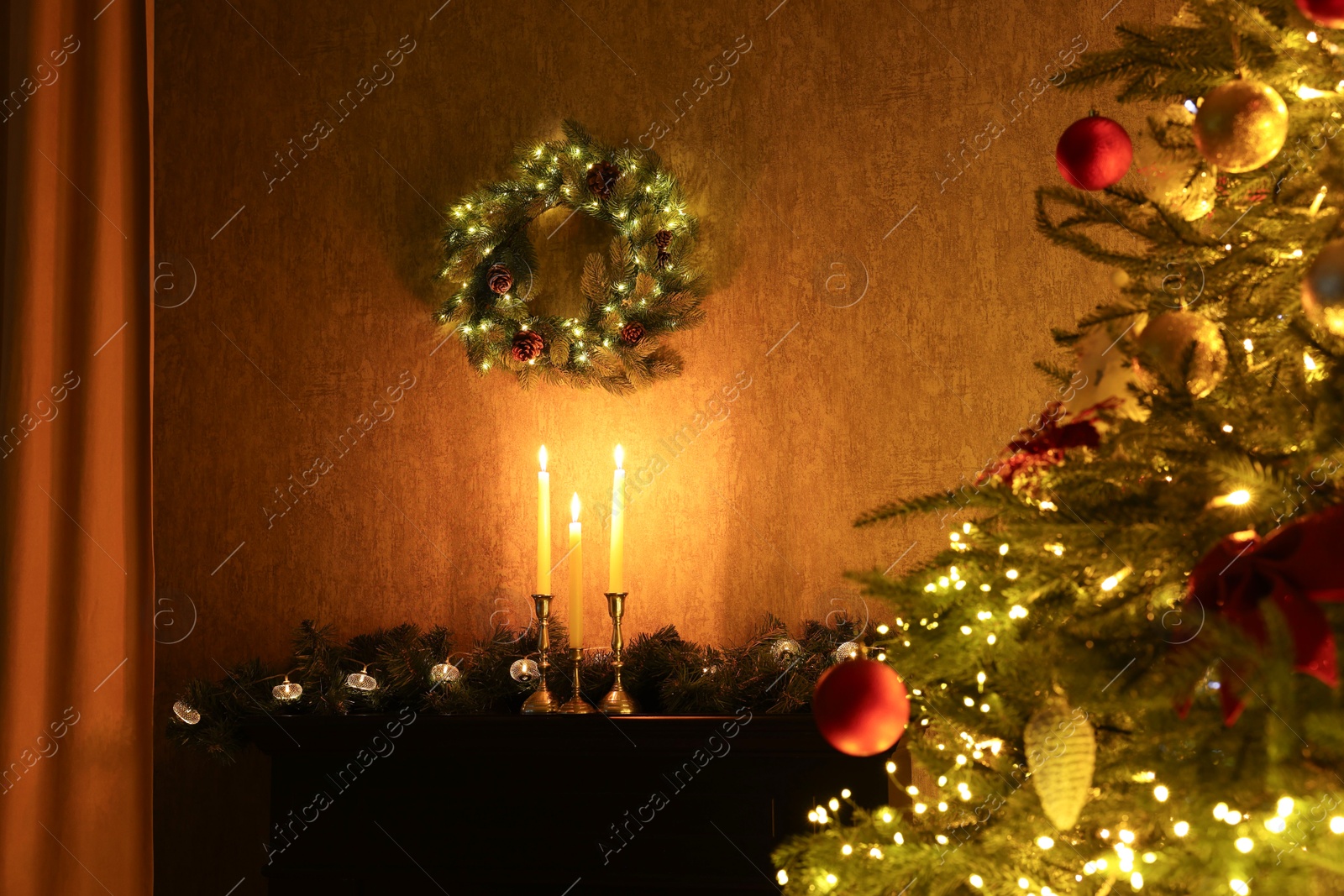 Photo of Beautifully decorated Christmas tree, burning candles, wreath and garland indoors