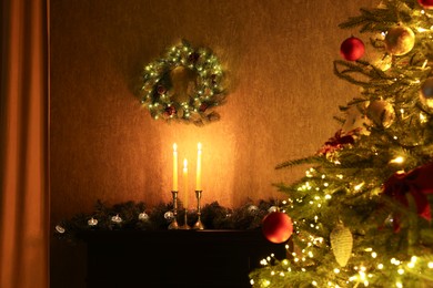 Photo of Beautifully decorated Christmas tree, burning candles, wreath and garland indoors