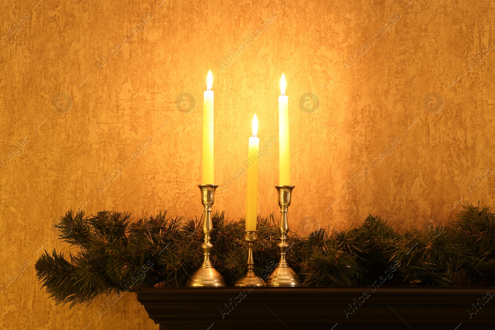 Photo of Burning candles and garland on shelf indoors. Christmas atmosphere