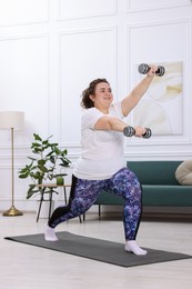 Photo of Plus size woman with dumbbells training at home